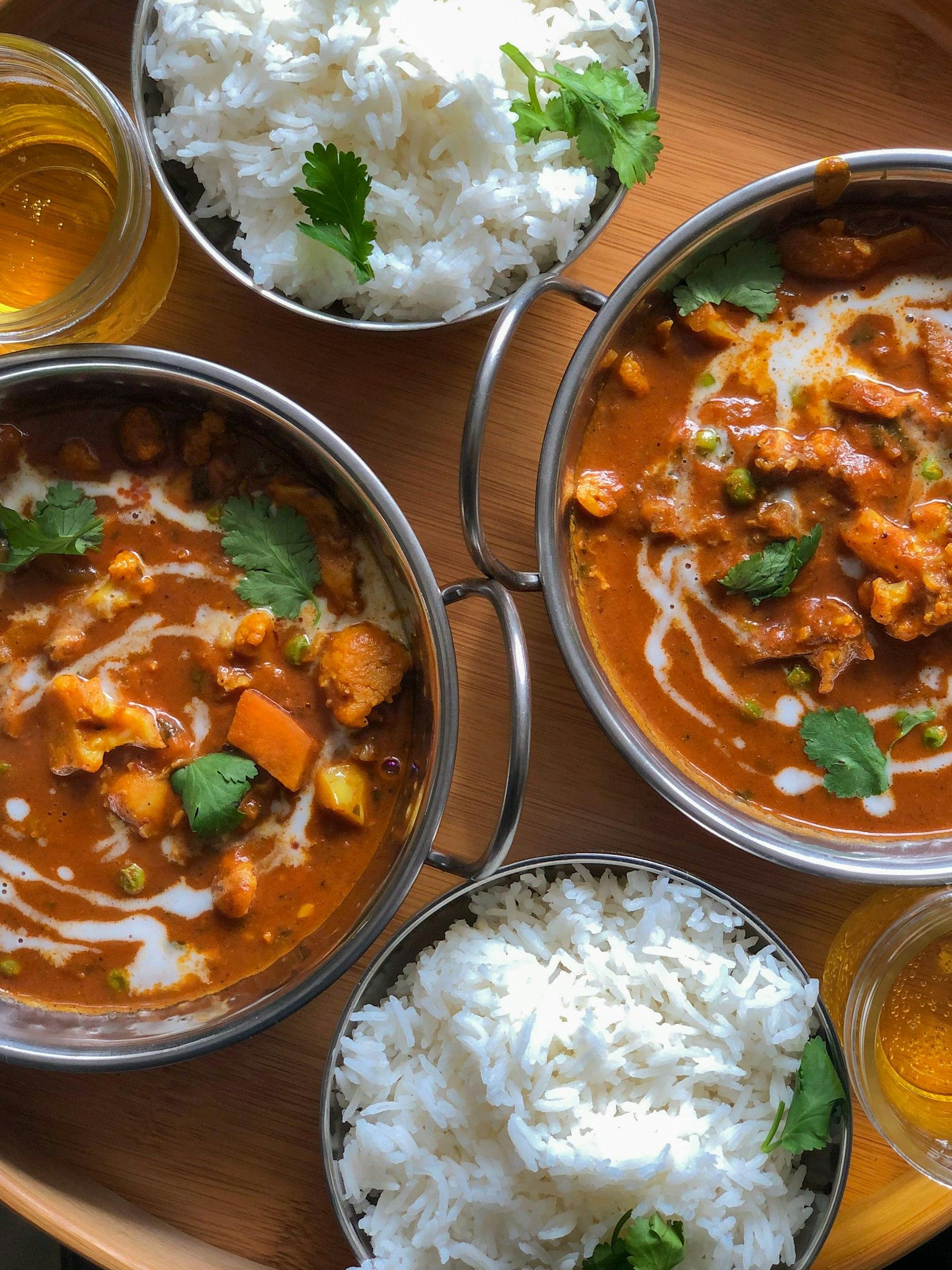 Two pots of slow-cooked curry with bowls of basmati rice