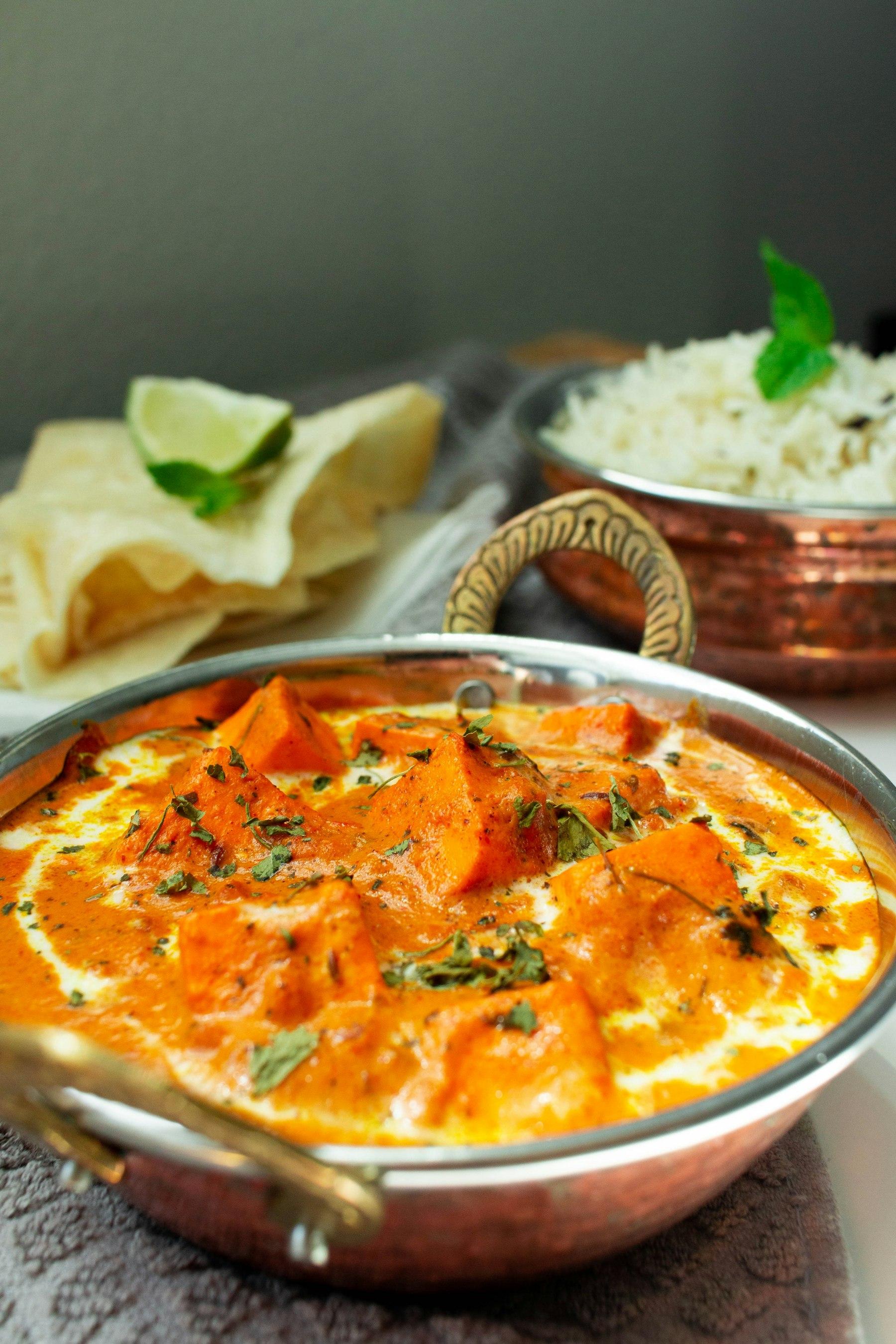 A creamy paneer curry in a copper pot with rice and breads